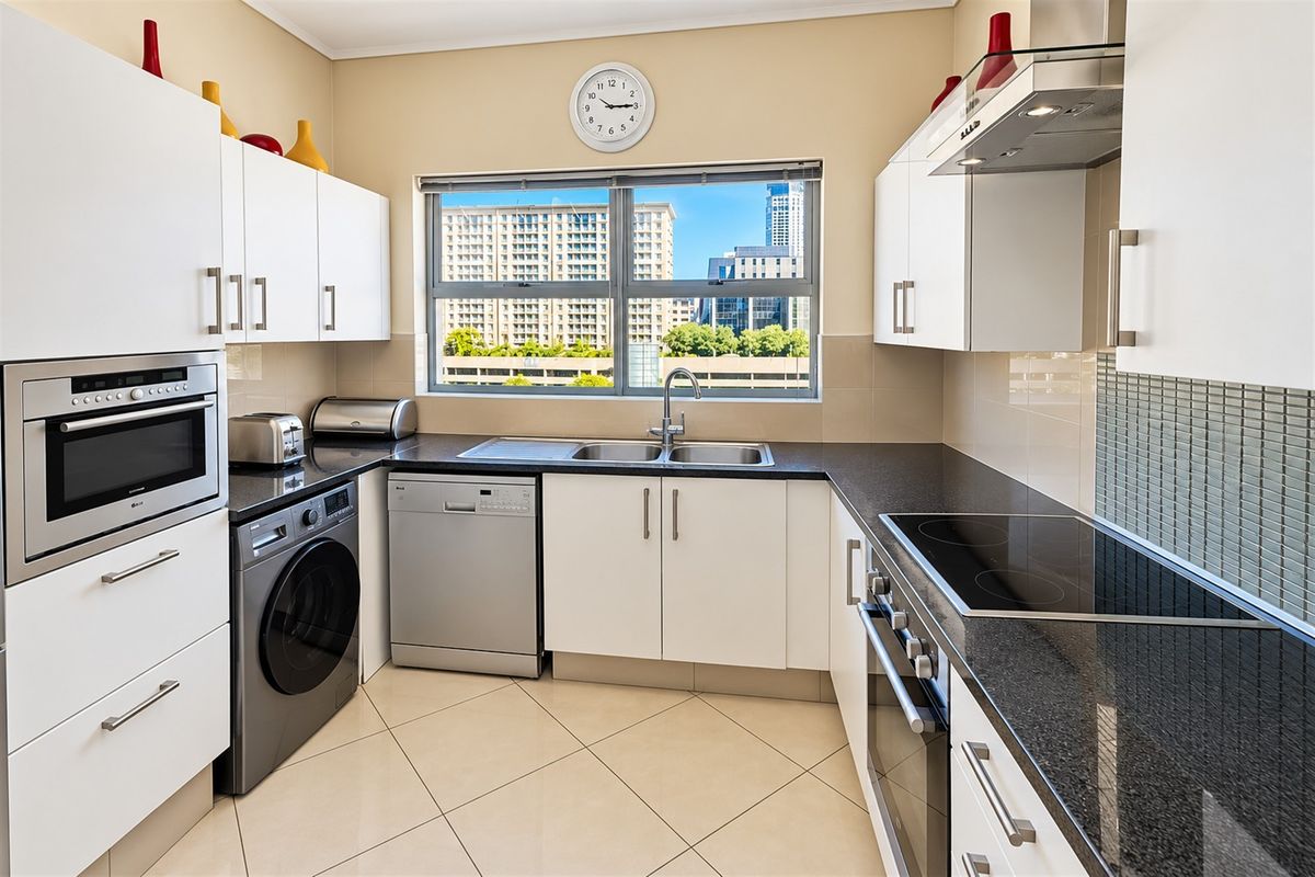 Modern kitchen featuring granite countertops, built-in oven, electric hob, extractor fan, and ample cabinetry, with a window providing natural light and urban views.