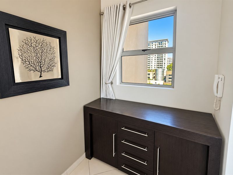 A compact office space featuring built-in dark wood cabinetry, an intercom system, and a window with views of the surrounding apartment complex.