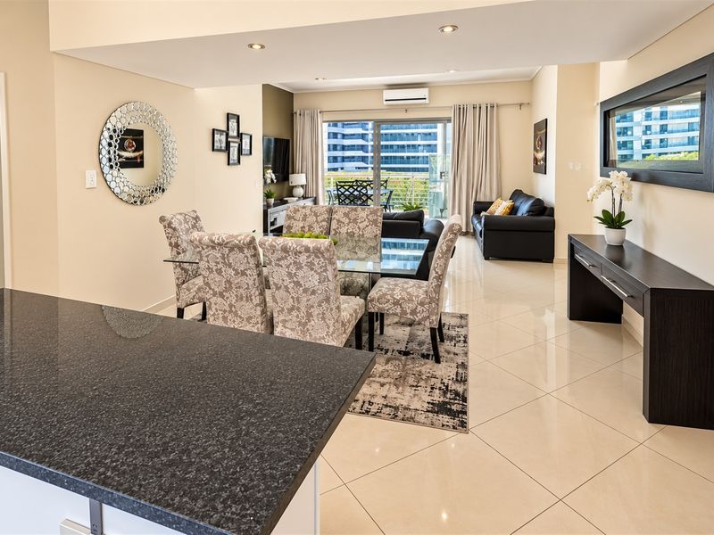 Spacious open-plan living and dining area featuring polished porcelain tiles, recessed lighting, and direct access to a private balcony through sliding glass doors.