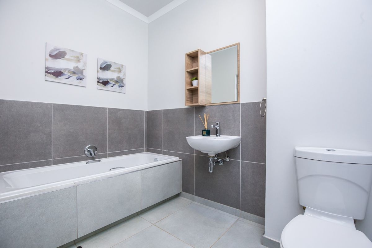 A modern, well-maintained bathroom featuring a built-in bathtub, wall-mounted basin, and toilet with neutral grey tiling.