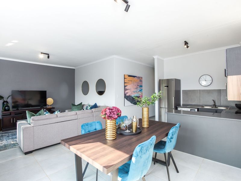 Modern open-plan living area featuring a contemporary kitchen with sleek cabinetry, tiled flooring, and integrated lighting, seamlessly flowing into the dining and lounge space.