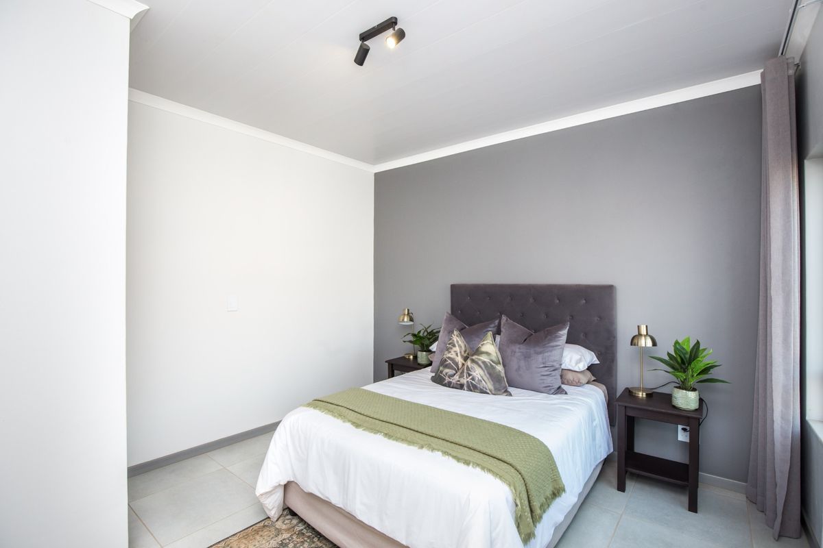 A well-maintained bedroom featuring neutral grey and white walls, tiled flooring, and modern track lighting.