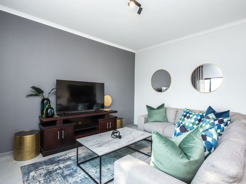 A well-maintained living room featuring a modern grey accent wall, neutral tiled flooring, and contemporary track lighting.