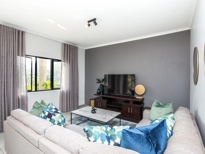 A well-maintained living room featuring a dark grey accent wall, neutral tiled flooring, and large windows with modern curtain tracks.