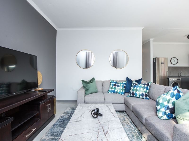 A modern open-plan living area featuring tiled floors, a striking grey accent wall, and a seamless transition into a functional kitchen space.