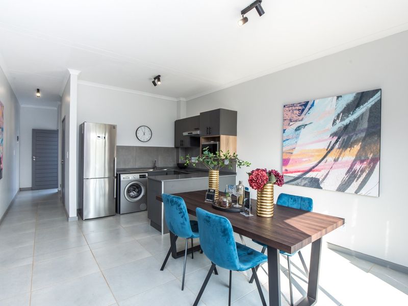 Modern open-plan kitchen and dining area featuring sleek cabinetry, tiled flooring, and contemporary track lighting in a well-maintained apartment setting.