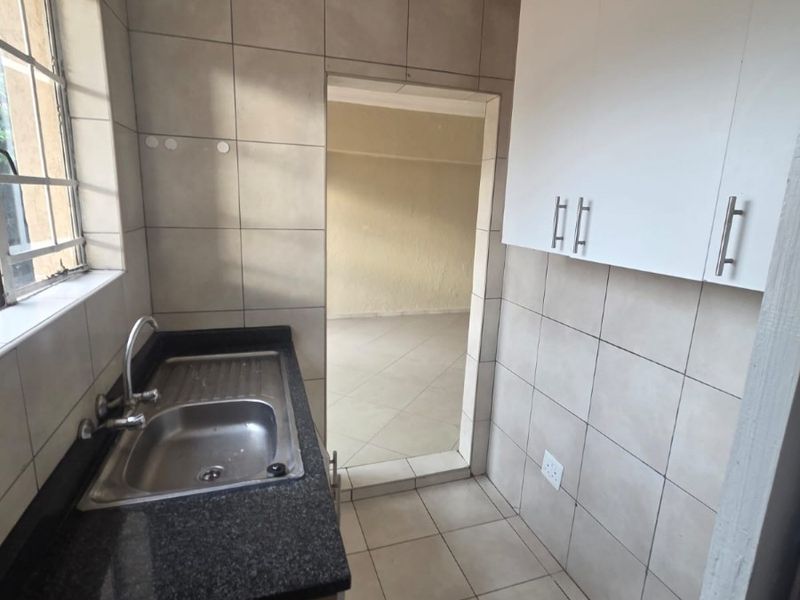 A functional scullery area featuring a stainless steel sink, granite countertop, tiled finishes, and wall-mounted cabinetry, providing a clean and practical utility space.