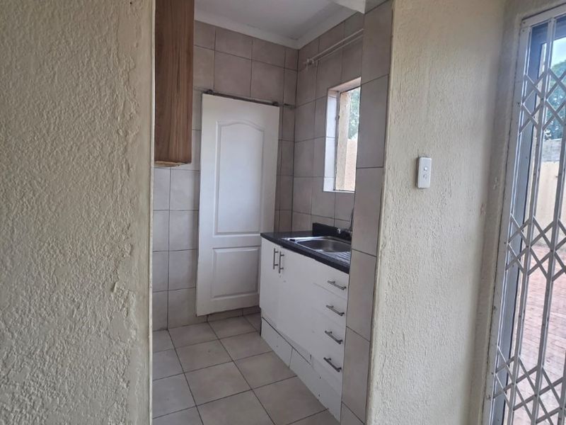 A compact scullery area featuring tiled flooring, built-in cabinetry with a sink, and tiled splashbacks, providing a functional secondary prep or wash-up space.