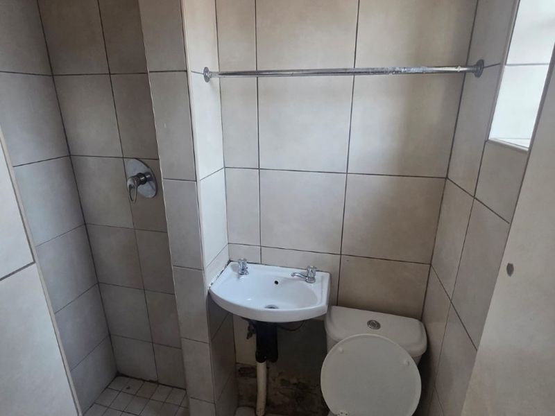 Compact bathroom featuring a shower, wall-mounted basin, and toilet with neutral wall and floor tiling.