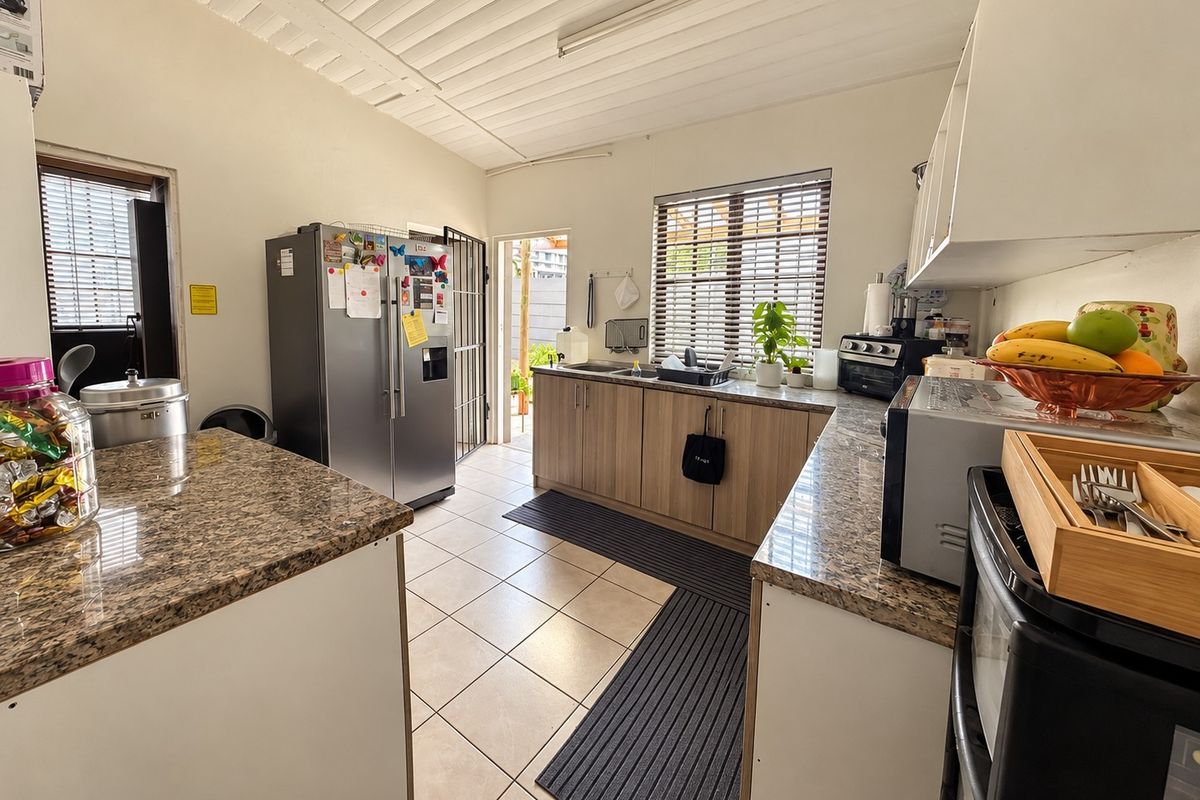 Functional kitchen featuring granite countertops, laminate cabinetry, tiled flooring, and direct access to the exterior via a security gate.