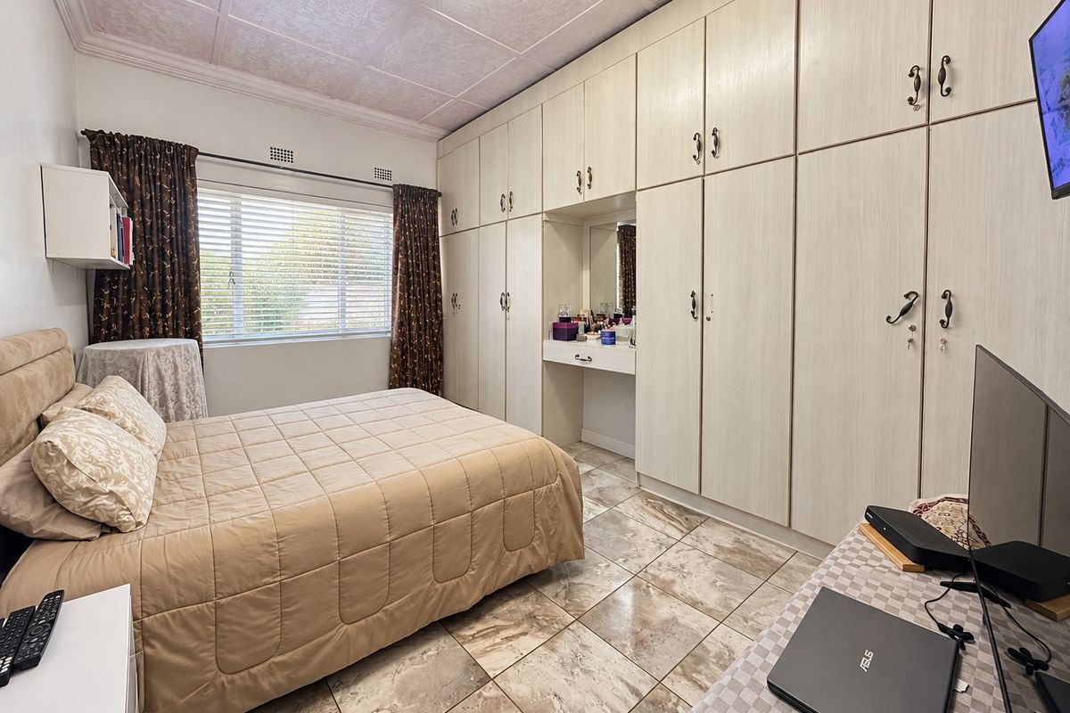 A bedroom featuring extensive built-in cabinetry with a vanity area, tiled flooring, and a window with venetian blinds.