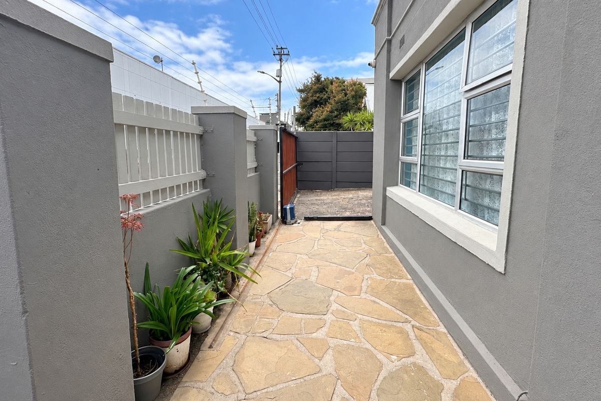 A side walkway featuring stone paving, enclosed by a boundary wall with security fencing and a gate.