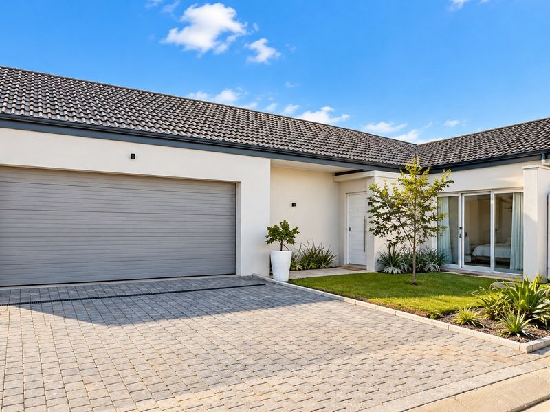 Modern single-story home featuring a paved driveway, automated garage, and a well-maintained front garden with a water tank.