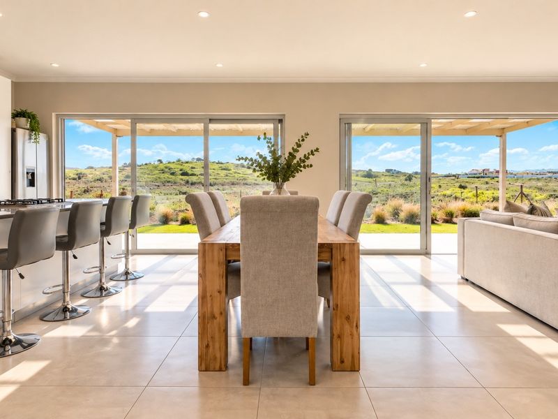 Modern open-plan living and dining area featuring a sleek kitchen island, tiled floors, and large sliding doors opening to a scenic landscape view.