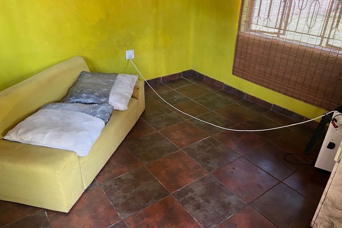 A living area featuring dark tiled flooring and bright yellow walls with security bars on the window.