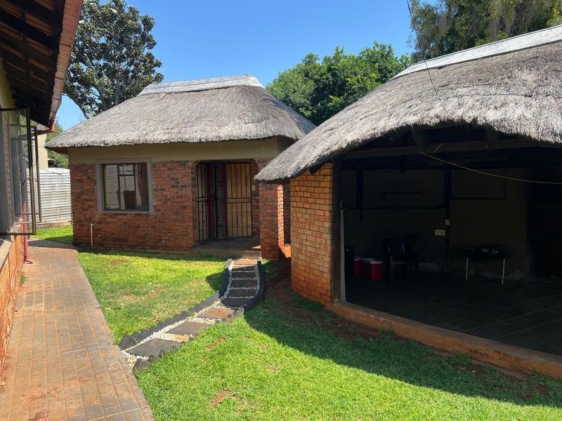 Rear view of the property featuring face brick structures with traditional thatch roofing, a paved walkway, and an open-air built-in braai area.