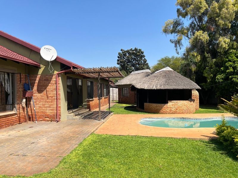 Rear garden featuring a swimming pool, a traditional thatched lapa, brick paving, and a wooden pergola attached to the main house.