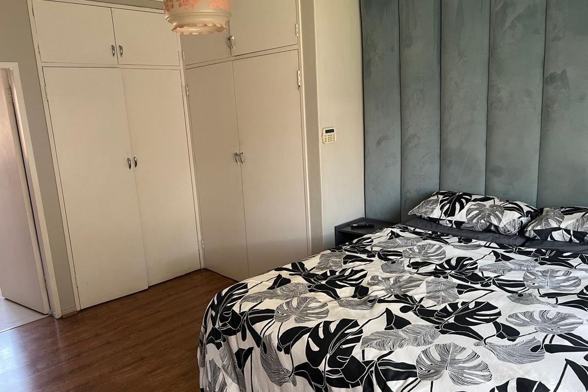 Bedroom featuring laminate flooring and extensive built-in cupboard storage with an integrated alarm system keypad.