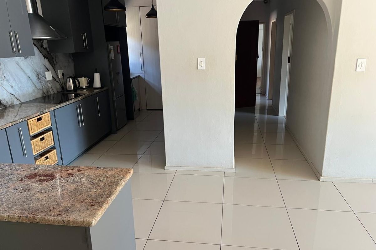 Modern kitchen featuring dark grey cabinetry, granite countertops, and polished ceramic floor tiles, leading through an elegant archway into the hallway.