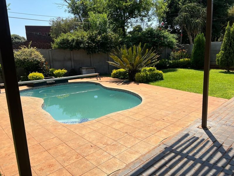 A well-maintained outdoor pool area featuring a tiled deck, landscaped garden, and a covered patio structure, perfect for outdoor relaxation and entertainment.