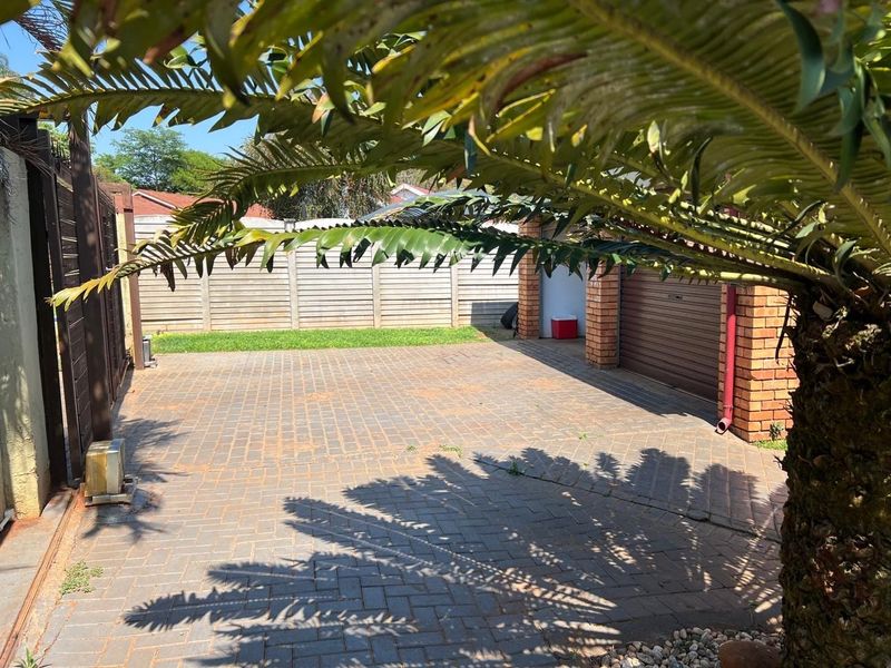 A paved driveway area featuring a brick boundary wall and a garage entrance, framed by mature garden foliage.