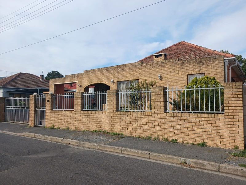 Front elevation of a face brick house featuring a secure boundary wall with metal fencing, tiled roof, and gated driveway access.