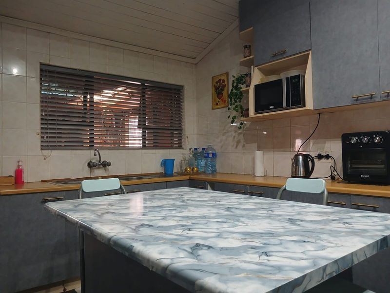 A functional kitchen featuring grey cabinetry, tiled backsplash, and a central island with a marble-effect countertop, providing ample workspace and storage.