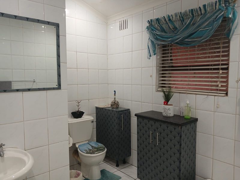 A functional bathroom featuring white wall tiles, a pedestal basin, a toilet, and built-in storage cabinetry with a patterned finish.