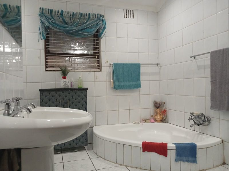 A dated bathroom featuring a corner bathtub, pedestal basin, and full-height wall tiling. The space offers a functional layout ready for modern updates.
