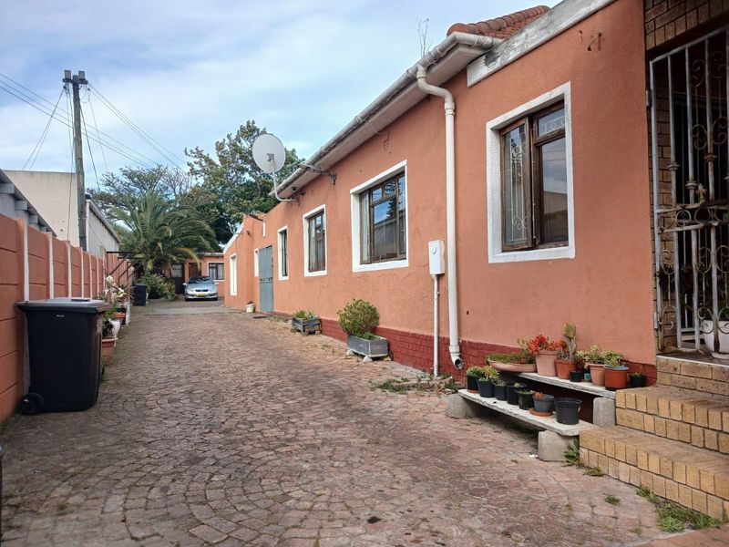 Rear exterior view of the property featuring a cobblestone driveway, brick steps, and security gate access.