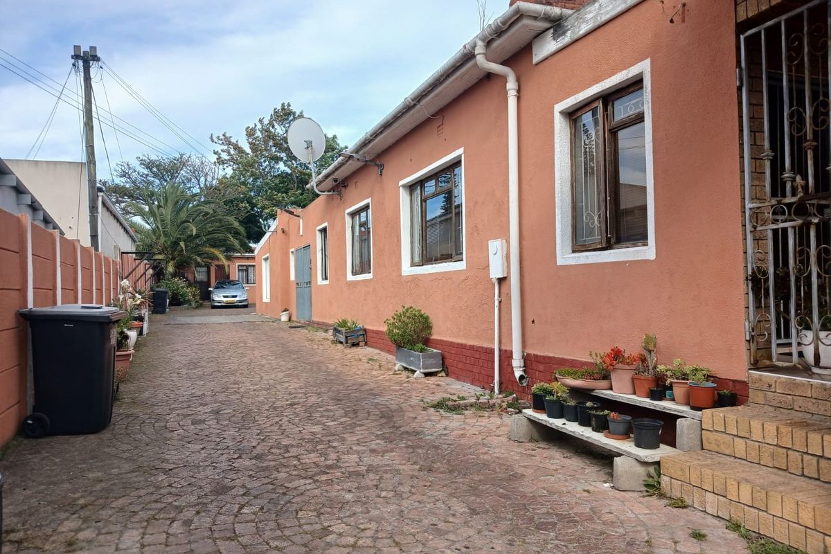 Rear exterior view of the property featuring a cobblestone driveway, brick steps, and security gate access.
