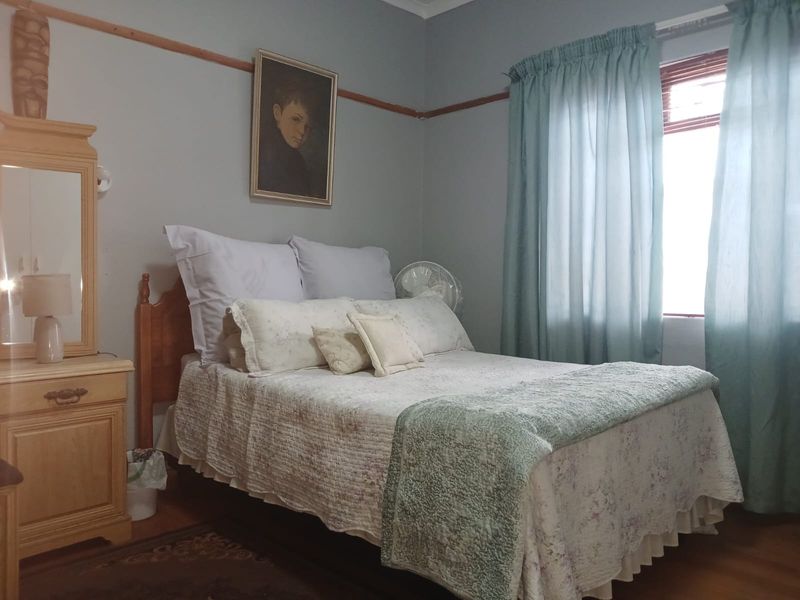 A cozy bedroom featuring timber flooring, a classic picture rail, and a window with natural light.