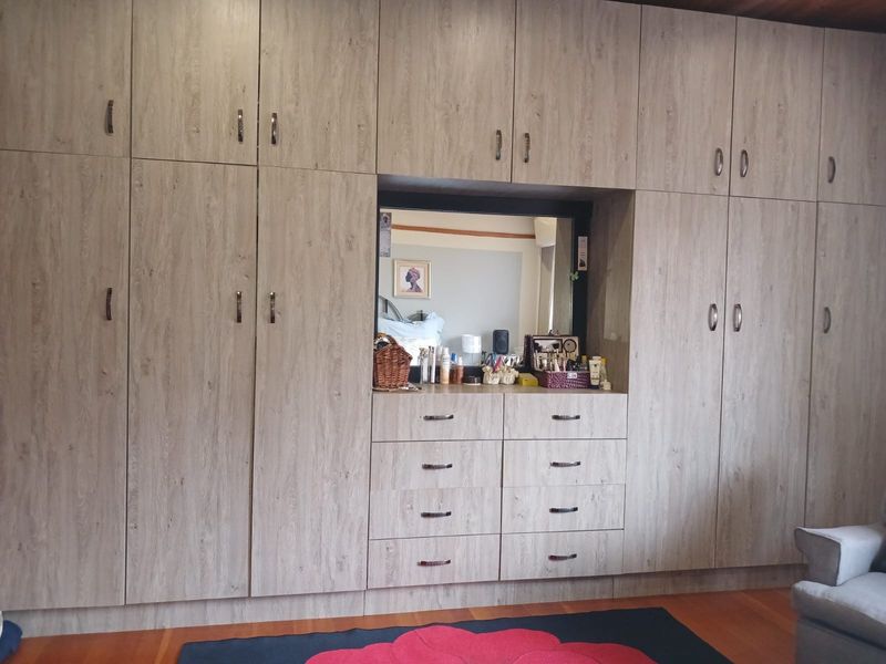A bedroom featuring extensive wall-to-wall built-in cupboards with integrated vanity, drawers, and mirror, finished in a light wood-grain laminate.