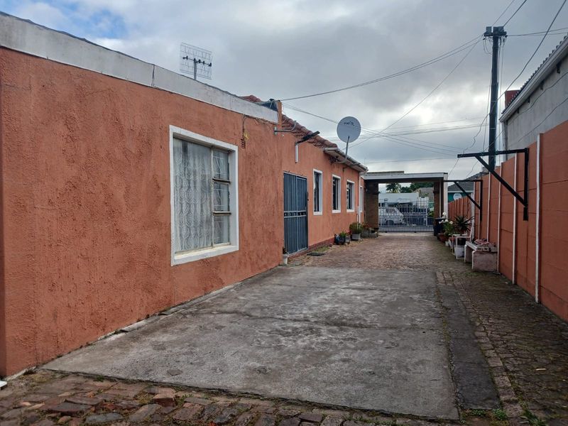 Rear exterior view of the property featuring a concrete driveway, brick boundary walls, and a metal security gate leading to the rear access area.
