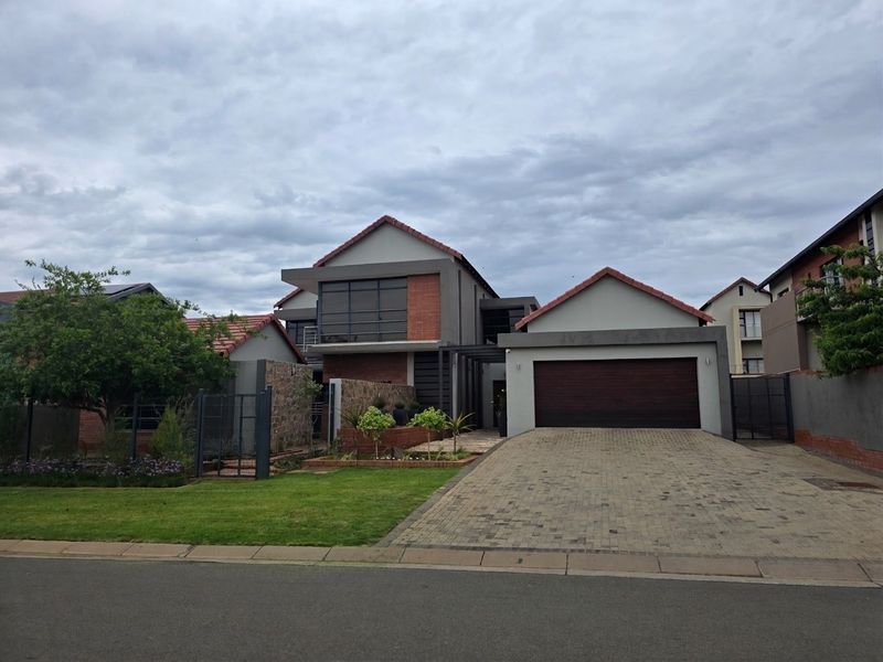 Modern double-storey residential home featuring a paved driveway, double garage, and attractive stone-clad facade with a well-maintained front garden.