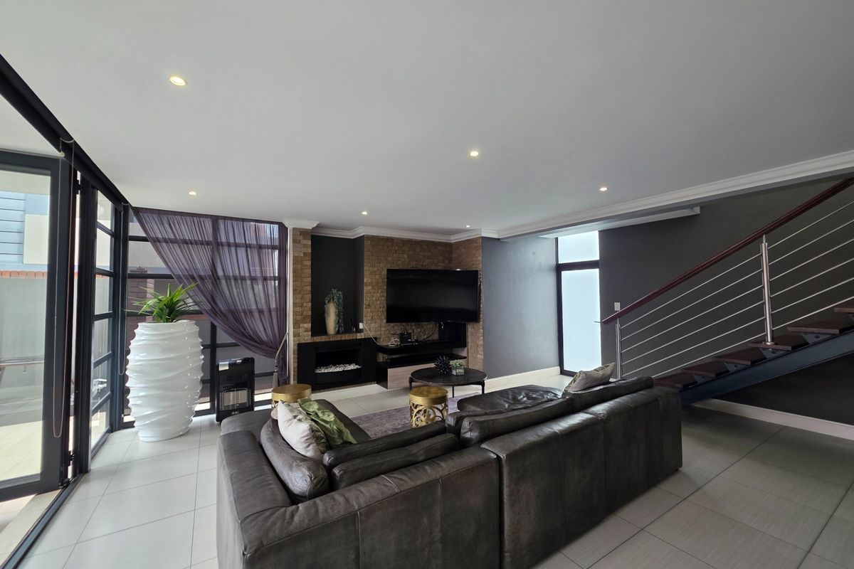 Modern living room featuring tiled floors, a built-in fireplace with an exposed brick feature wall, and a staircase with a contemporary metal railing.