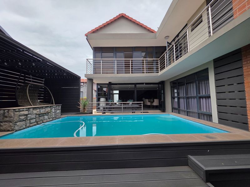Modern outdoor entertainment area featuring a swimming pool, timber decking, stone-clad feature wall, and a covered patio with access to the main residence.