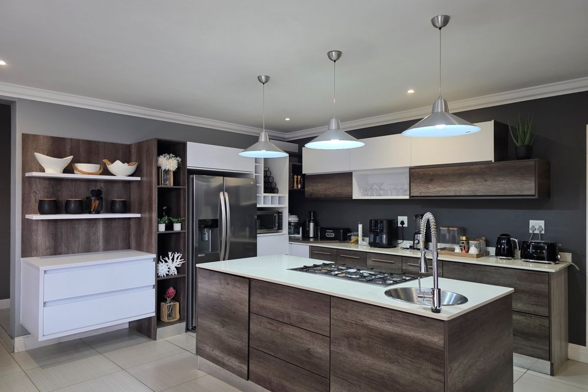 Modern kitchen featuring a central island with a gas hob and sink, sleek two-tone cabinetry, and contemporary pendant lighting.