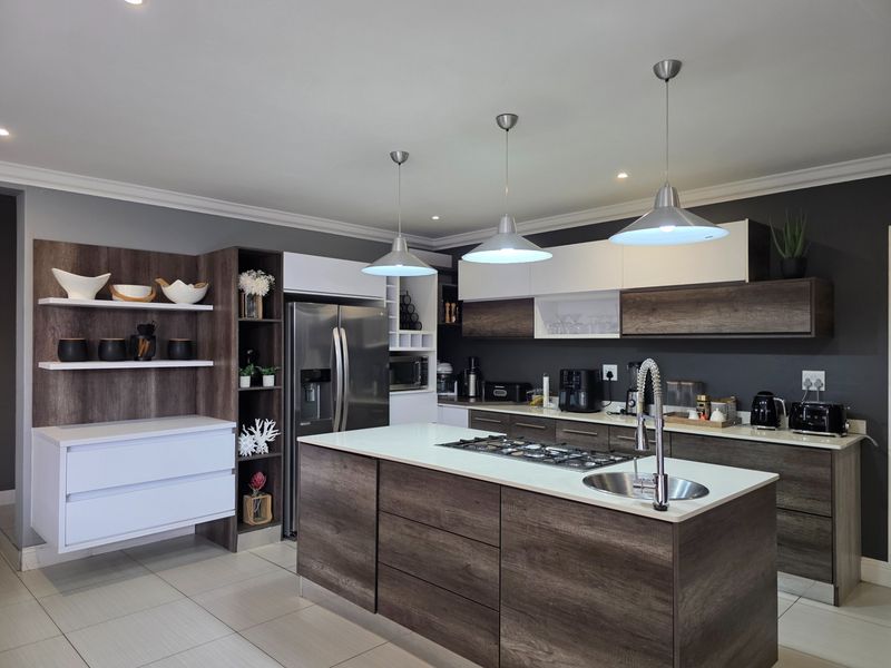 Modern kitchen featuring a central island with a gas hob and sink, sleek two-tone cabinetry, and contemporary pendant lighting.