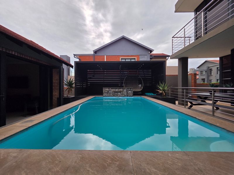 A well-maintained swimming pool area featuring a stone-clad water feature, timber pergola, and modern stainless steel balustrades, perfect for outdoor relaxation and entertainment.