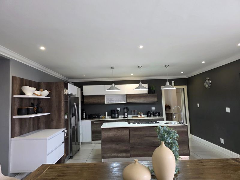 Modern kitchen featuring a central island with a gas cooktop, sleek two-tone cabinetry, and contemporary pendant lighting, finished with high-quality tiled flooring.