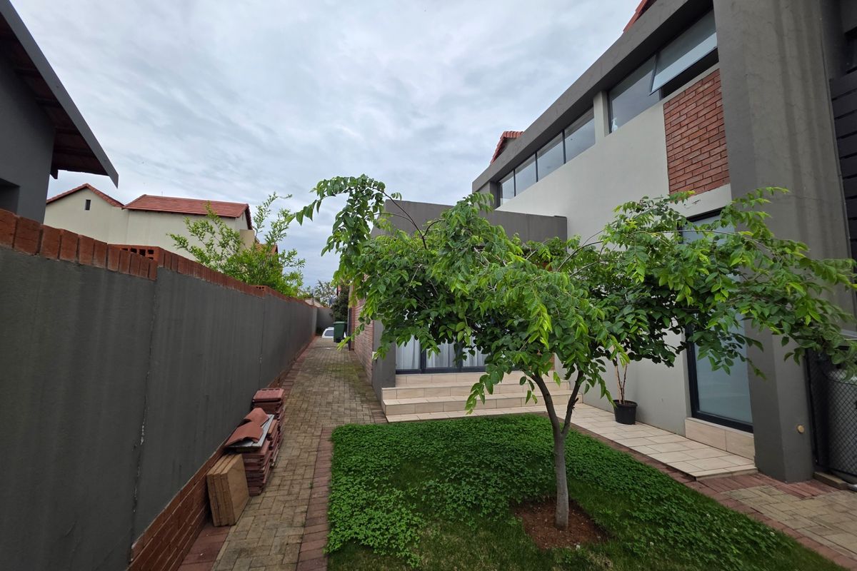 A view of the rear exterior featuring a paved walkway, small lawn area, and modern multi-story building facade with brick and plaster finishes.