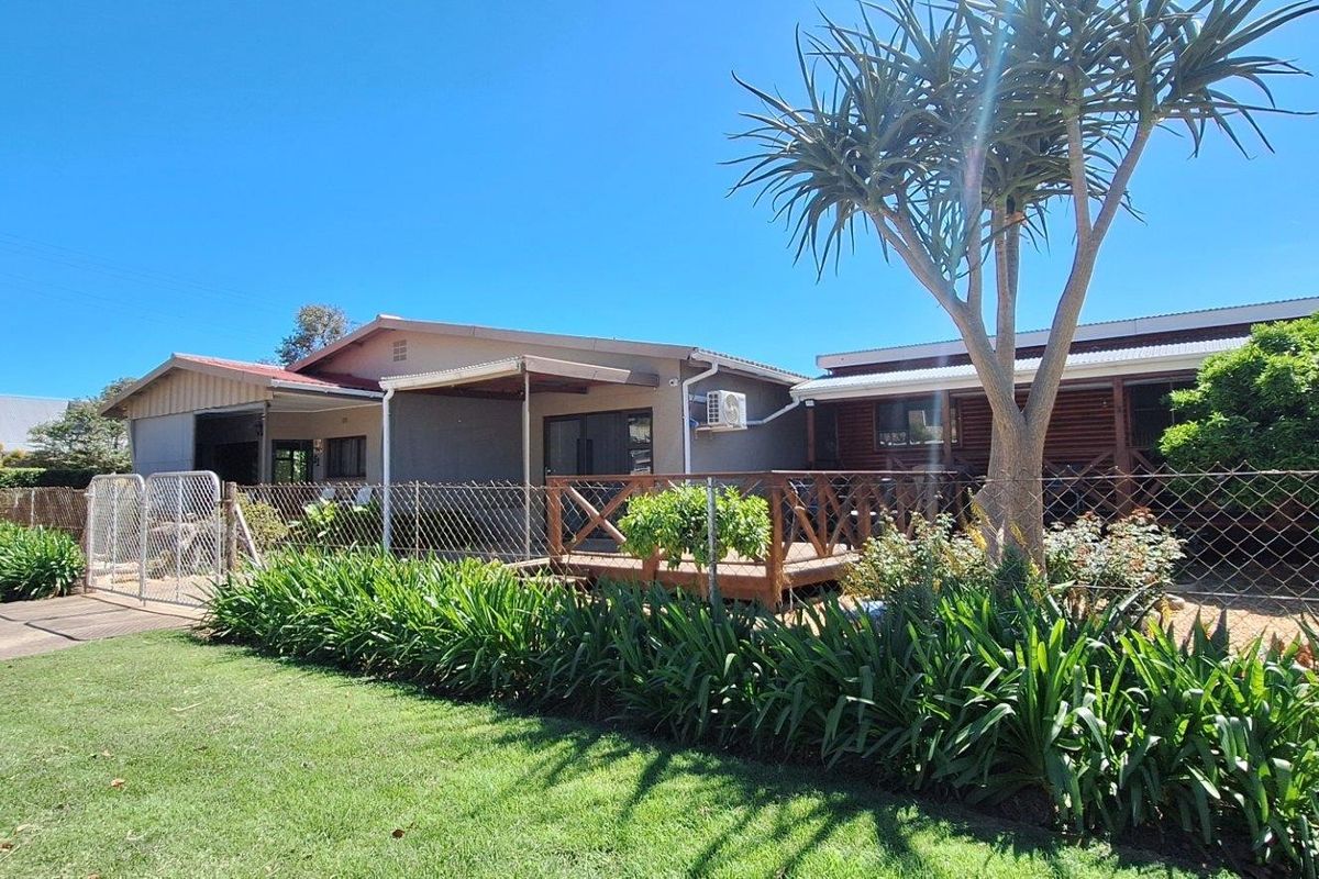 Rear view of the property featuring a wooden deck, covered patio area, and a well-maintained garden enclosed by chain link fencing.