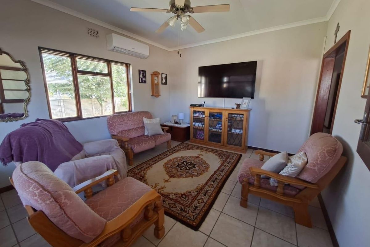 A comfortable living room featuring tiled flooring, a ceiling fan, and a wall-mounted air conditioning unit, providing a functional and well-maintained space.