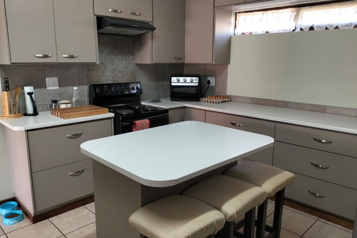 A functional kitchen featuring grey built-in cabinetry, laminate countertops, an electric stove with extractor fan, and a central island with seating.