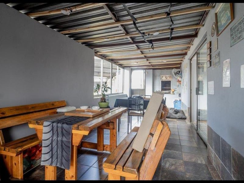 Covered patio area featuring tiled flooring, a built-in braai, and an exposed beam ceiling, providing a functional space for outdoor entertaining.