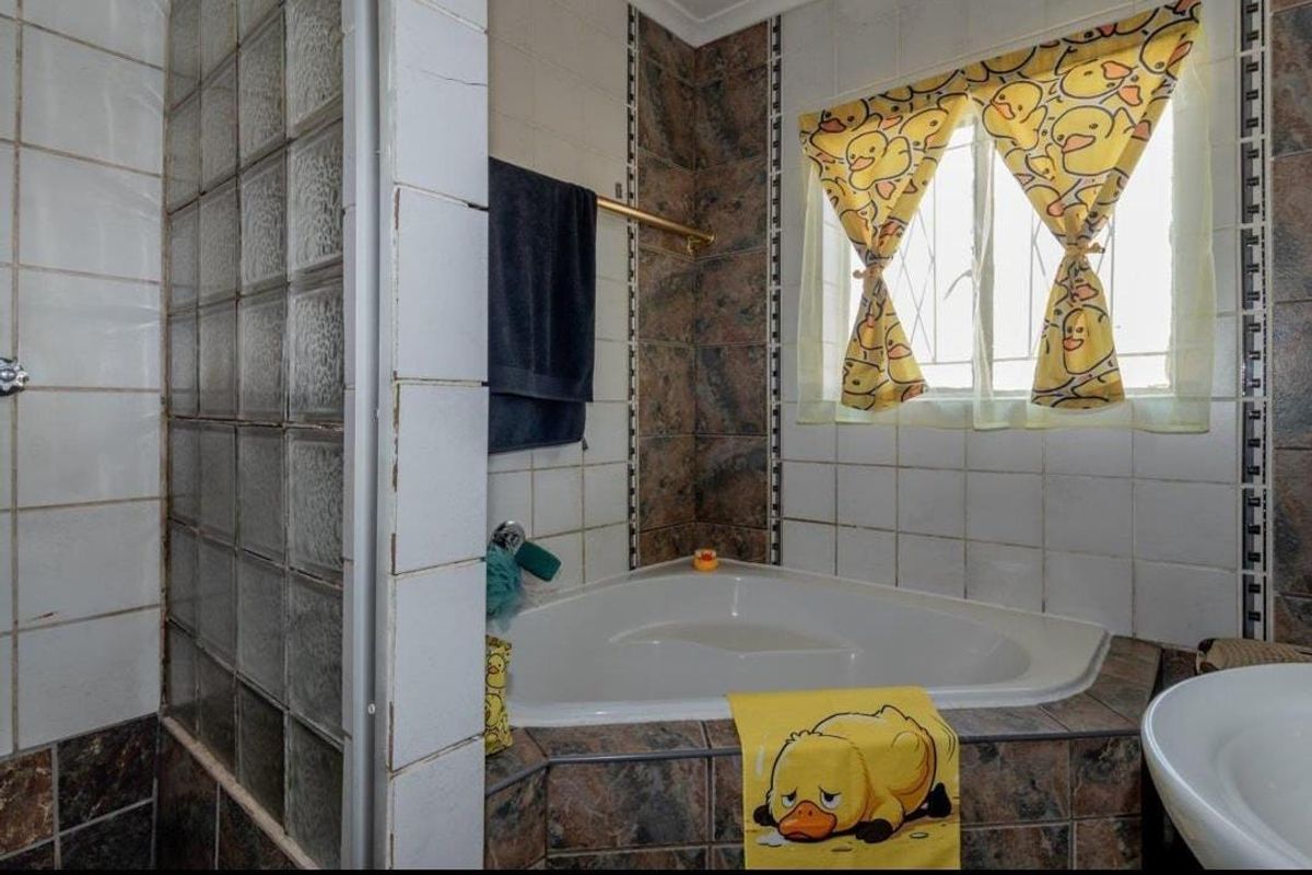 Bathroom featuring a corner bathtub, glass block shower partition, and tiled finishes. The space would benefit from modern updates to the tiling and fixtures.