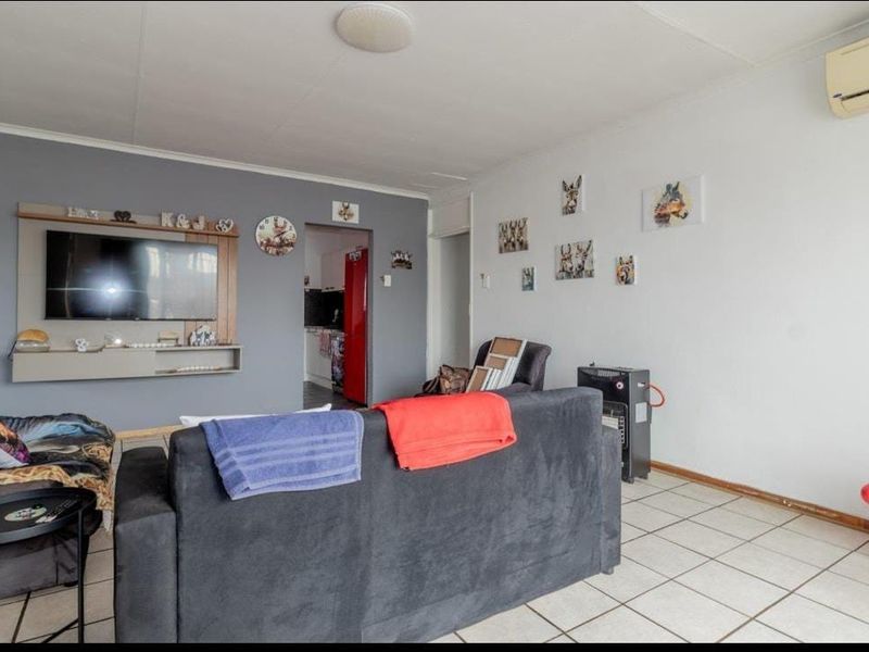 A functional living room featuring tiled flooring, a wall-mounted air conditioning unit, and a built-in media console area.