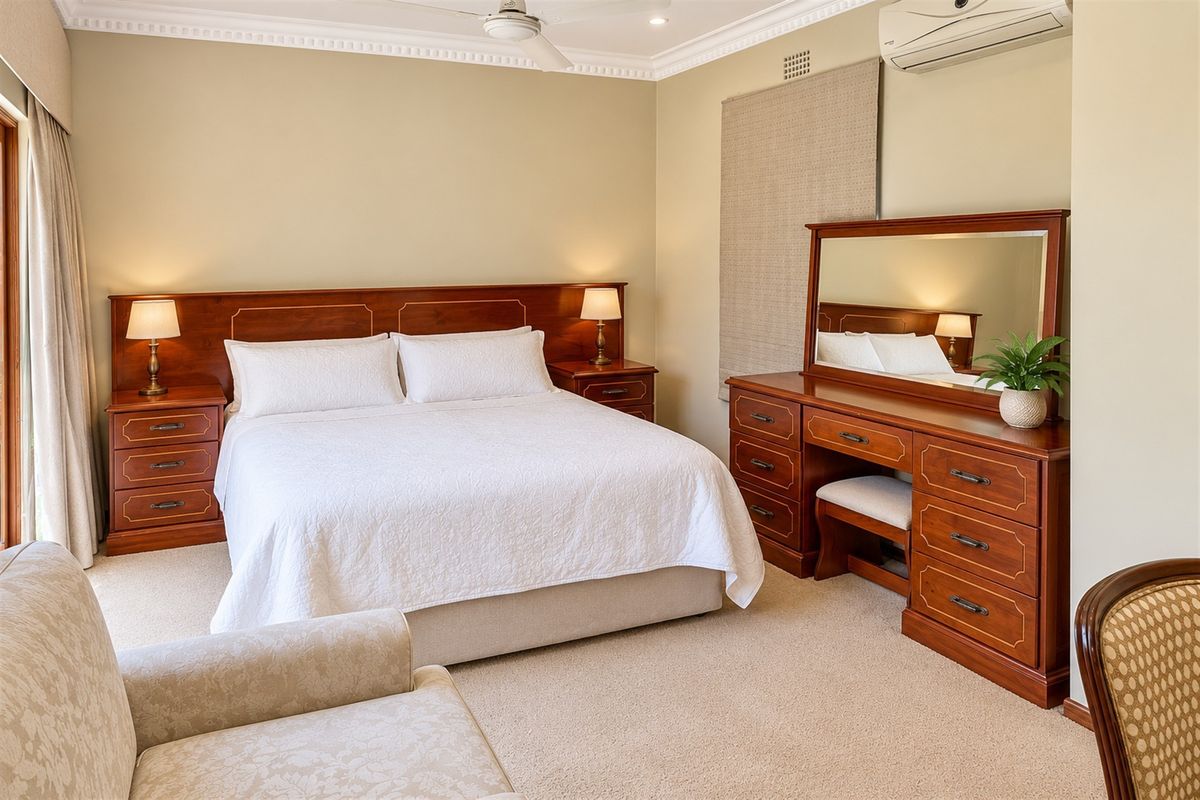 A well-maintained bedroom featuring neutral wall tones, carpeted flooring, a ceiling fan, and a wall-mounted split system air conditioner.