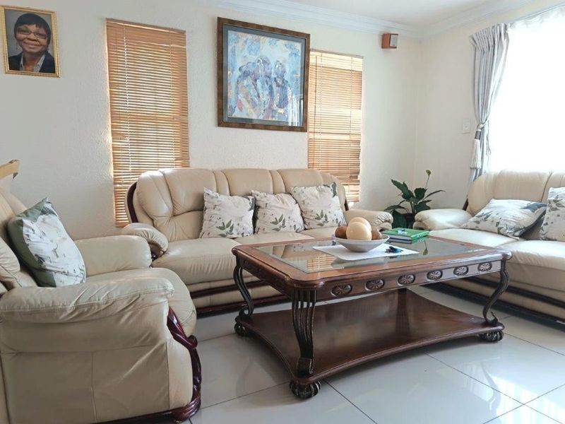 A bright and well-maintained living room featuring neutral tiled flooring, coved ceilings, and venetian blinds on the windows.